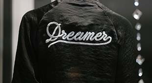 A person poses so that the back of their jacket is center frame. The jacket is emblazoned with the word "Dreamer".