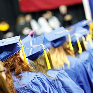 Graduates in blue robes march down the aisle towards the stage