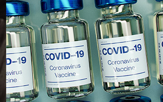 A close up of a row of test tubes. They are labeled 'COVID-19 Coronavirus Vaccine'.
