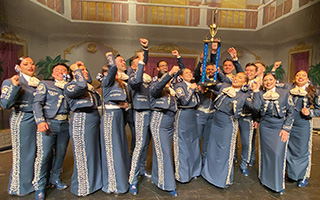 CSN's Mariachi band stand together in celebration. Two members at the front of the group hoist a trophy high above their heads.