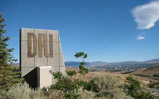 The DRI sign, angular stone with bronze metallic letters, stands against a bright blue Nevada sky.