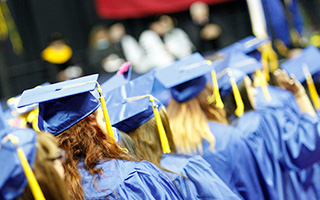 A high-angle shot of graduates in blue caps walking in a line during a commencement ceremony.