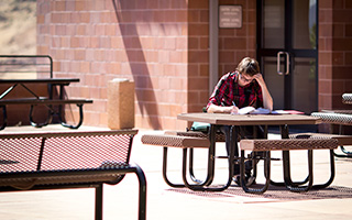 A TMCC student sits at an outdoor picnic table with an open book, taking notes.