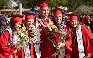A group of five graduates in red caps and gowns do a group pose for the camera.