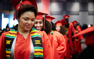 A line of African-American graduates in red robes walk down the aisle during a commencement ceremony.