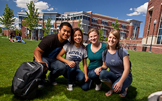 A group of four students pose together on a grassy field.