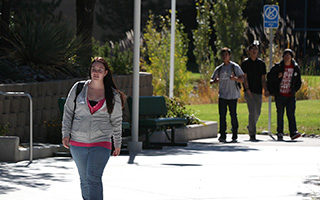 A student walks through the quad of the WNC campus. Three other students walk together in the background.