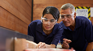 an older worker supervises a younger worker during a manufacturing operation.