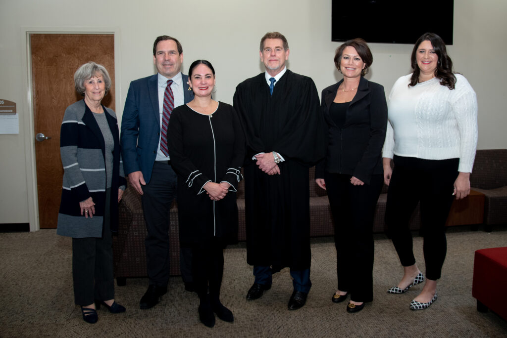 Five NSHE Regents pose for a picture in a conference room. A judge stands in the center of the regents wearing black robes.