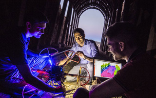 UNR researchers work with quadcopter drones and a laptop within a darkened tunnel.