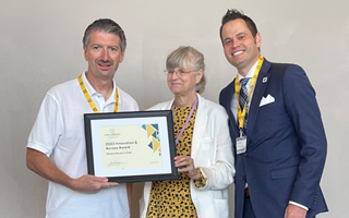 WNC President Kyle Dalpe poses with a framed certificate. A woman in a white blazer and a man in a blue blazer stand close by.