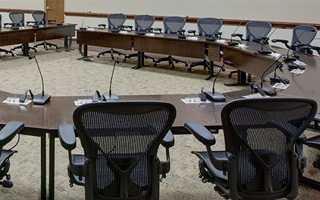 A boardroom featuring a horseshoe shaped table. All chairs are empty