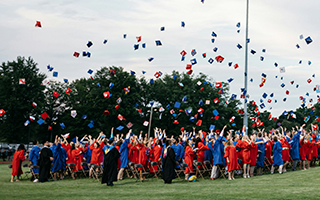 Image of large group of high school graduates wearing red and blue gowns.