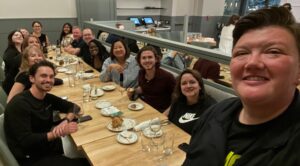 Dinner with Yali2 A smiling person in the foreground takes a selfie in a dining hall. Behind them a large group also smile for the camera.