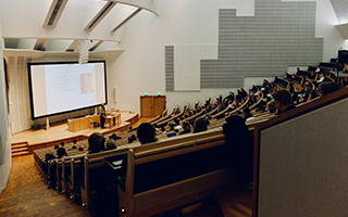 Image of a large lecture hall with students listening attentively to the lecturer.
