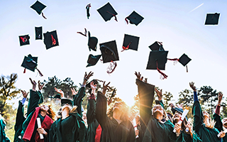 Crowd of smiling graduates throwing caps in the air.