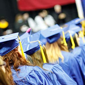 Graduates clad in blue caps and gowns walk towards a stage during commencement
