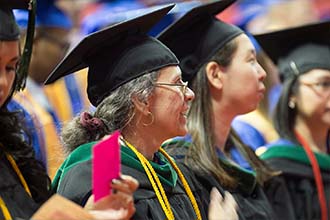 A graduate with a beaming smile sits amongst a crowd of other grads during commencement