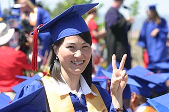 A graduate in a blue cap and gown flashes a peace sign at the camera