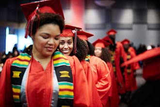 UNLV graduates in red gowns walk in a line towards the camera