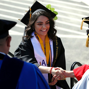 Graduates clad in blue caps and gowns walk towards a stage during commencement