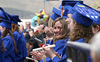 A crowd shot of graduates waring blue robes. A smiling woman is in focus