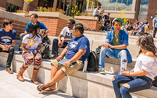 A diverse group of students engage in conversation while seated in an outdoor amphitheater.