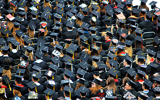 Large of graduates with black graduation caps and gowns sitting in rows.