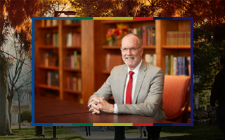 Image of UNLV President Chris Heavey sitting framed in NSHE colors and a darker fall background of campus.